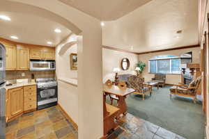 Kitchen featuring light brown cabinets, stone tile flooring, arched walkways, and appliances with stainless steel finishes