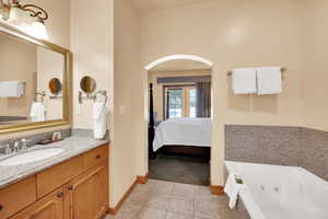 Ensuite bathroom with vanity, a whirlpool tub, tile patterned flooring, ensuite bath, and baseboards