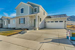 Traditional home featuring stone siding, an attached garage, board and batten siding, and concrete driveway