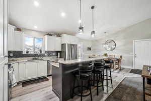Kitchen with decorative backsplash, a kitchen island, appliances with stainless steel finishes, a sink, and vaulted ceiling