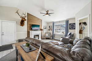 Living room with baseboards, lofted ceiling, a fireplace, and a ceiling fan