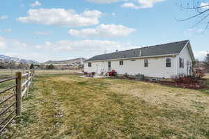 Back of property featuring fence, a mountain view, a patio area, and a lawn