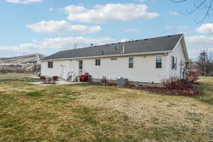 Rear view of property featuring roof with shingles, central AC unit, a mountain view, a yard, and a patio area