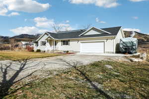 Single story home with roof with shingles, an attached garage, a front lawn, gravel driveway, and a mountain view
