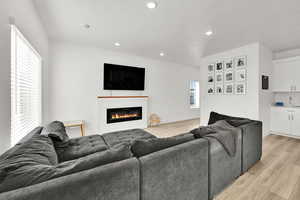 Living room featuring light wood-style flooring, a glass covered fireplace, baseboards, and recessed lighting
