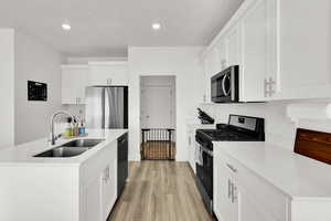 Kitchen with light countertops, appliances with stainless steel finishes, white cabinetry, a sink, and light wood-type flooring