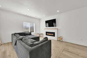 Living area featuring a glass covered fireplace, a textured ceiling, light wood-style flooring, baseboards, and recessed lighting
