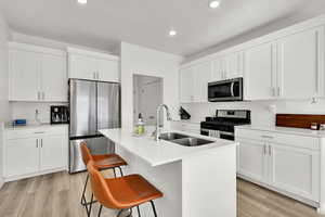 Kitchen with light wood-type flooring, stainless steel appliances, a sink, an island with sink, and white cabinets