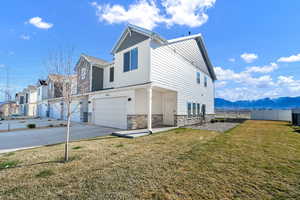 View of side of property with concrete driveway, fence, an attached garage, stone siding, and a lawn