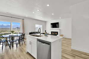 Kitchen with open floor plan, a sink, stainless steel dishwasher, and light wood finished floors