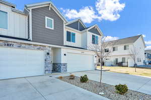 View of front of property with driveway, stone siding, an attached garage, board and batten siding, and a residential view