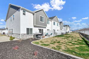 Back of property featuring stone siding, fence, a lawn, and a patio