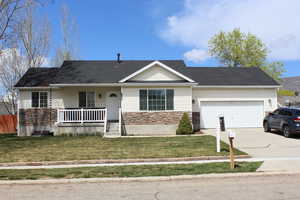 Single story home featuring concrete driveway, stone siding, an attached garage, a porch, and a front lawn