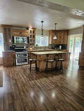 Kitchen with stainless steel appliances, dark wood-type flooring, a breakfast bar, backsplash, and brown cabinetry