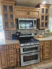 Kitchen featuring brown cabinetry, appliances with stainless steel finishes, light wood-style floors, light stone counters, and backsplash