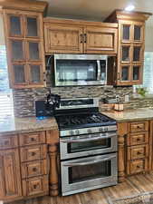 Kitchen featuring light wood-style flooring, appliances with stainless steel finishes, light stone counters, brown cabinets, and backsplash