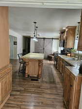 Kitchen with stainless steel appliances, dark wood-type flooring, a kitchen island, a sink, and light stone countertops