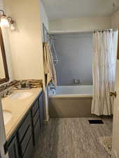 Bathroom with double vanity, a sink, shower / tub combo, and wood finished floors