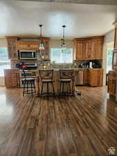 Kitchen with dark wood-type flooring, decorative backsplash, brown cabinetry, and appliances with stainless steel finishes