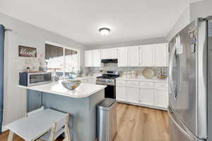 Kitchen with light wood-type flooring, under cabinet range hood, decorative backsplash, a peninsula, and appliances with stainless steel finishes