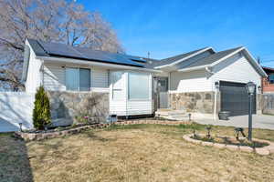 View of front facade with stone siding, a front yard, a garage, and roof mounted solar panels