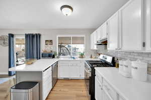 Kitchen featuring white cabinets, a peninsula, under cabinet range hood, and stainless steel appliances