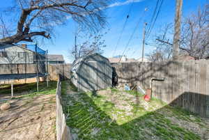 View of yard featuring a fenced backyard, a storage shed, an outdoor structure, and a trampoline