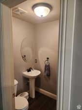 Half bathroom with visible vents, baseboards, toilet, wood finished floors, and a sink