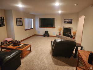 Living room with arched walkways, carpet flooring, a tiled fireplace, and baseboards