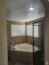 Full bathroom featuring a shower stall, a textured ceiling, a jetted tub, and vanity