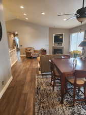 Dining room with wood finished floors, baseboards, ceiling fan, vaulted ceiling, and a tiled fireplace