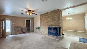 Unfurnished living room featuring a textured ceiling, visible vents, carpet, a stone fireplace, and ceiling fan with notable chandelier