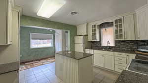 Kitchen with a sink, a center island, glass insert cabinets, white appliances, and decorative backsplash