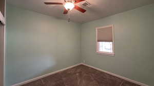 Spare room featuring a ceiling fan, baseboards, dark colored carpet, and visible vents