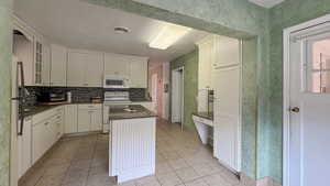 Kitchen featuring decorative backsplash, light tile patterned flooring, glass insert cabinets, and white appliances