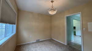 Carpeted empty room with baseboards, visible vents, a chandelier, and tile patterned floors