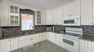 Kitchen with tasteful backsplash, decorative light fixtures, white appliances, a sink, and glass insert cabinets