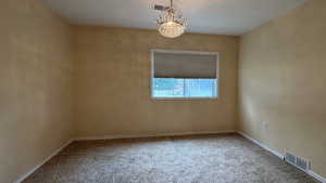 Carpeted spare room with baseboards, visible vents, and a notable chandelier