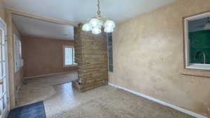 Carpeted empty room with tile patterned floors, a notable chandelier, a textured ceiling, baseboards, and a textured wall