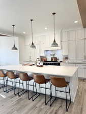 Kitchen with a large island with sink, light countertops, white cabinetry, light wood-type flooring