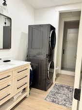 Laundry area featuring light wood-style flooring, stacked washer / dryer, and full bathroom with walk-in shower.