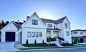 View of front of house featuring roof with shingles, a standing seam roof, board and batten siding, an attached garage, and driveway