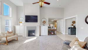 Living area with baseboards, a high ceiling, light carpet, a tile fireplace, and ceiling fan