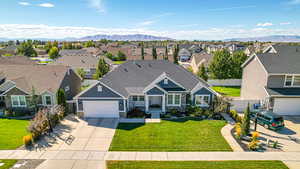 Traditional-style house featuring concrete driveway, fence, stone siding, a residential view, and a front yard