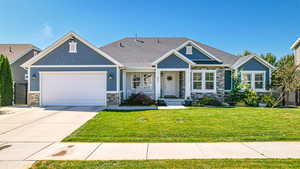 Craftsman-style home with driveway, a front yard, stone siding, roof with shingles, and a garage