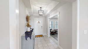 Foyer with light tile patterned floors, a tray ceiling, baseboards, and a chandelier