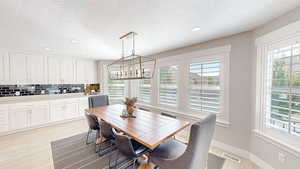 Dining area featuring a textured ceiling, visible vents, light wood finished floors, baseboards, and a notable chandelier
