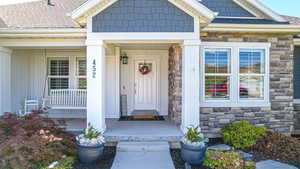 Doorway to property featuring stone siding, board and batten siding, a porch, and roof with shingles