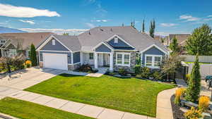 View of front of house featuring concrete driveway, fence, an attached garage, stone siding, and a front lawn