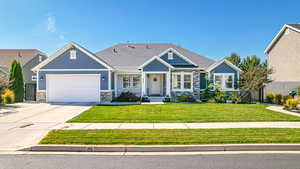 Craftsman-style house with stone siding, a front yard, driveway, and a garage